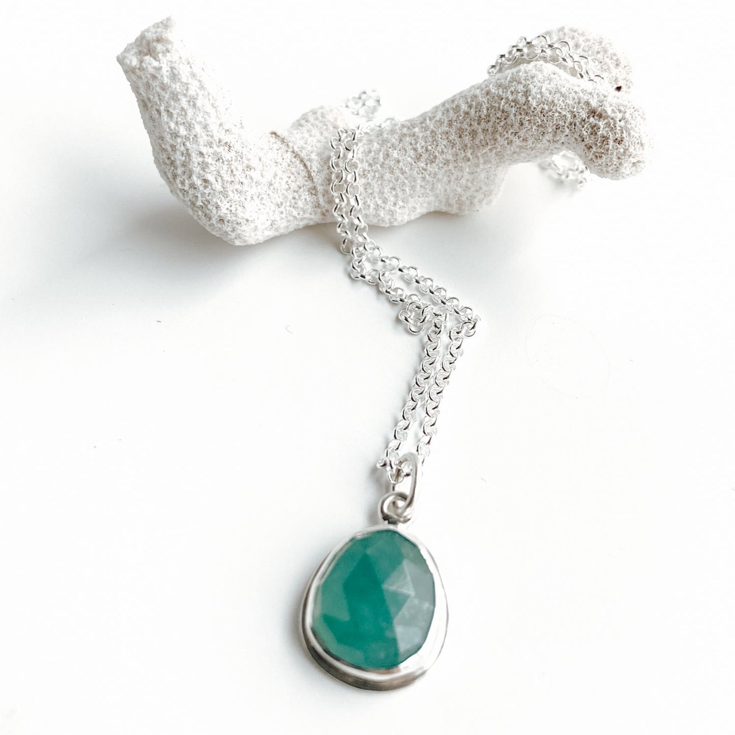 Rosecut Gandiderite gemstone and silver pendant sitting on a white background with a piece of white coral
