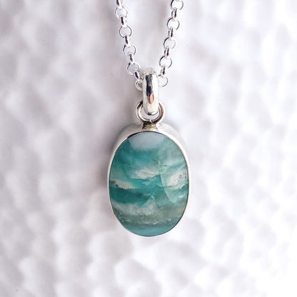 Close up view of the silver bezel set teal and aqua opalized wood gemstone pendant against a white textured background