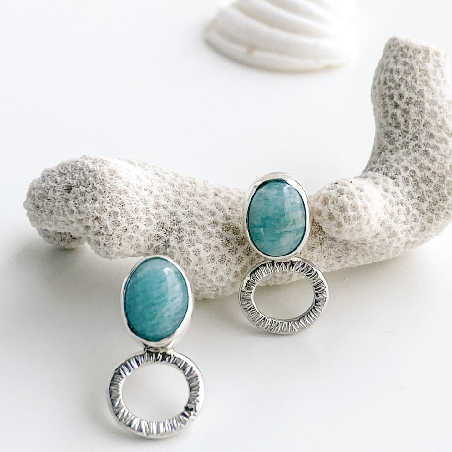 Closeup view of ocean blue amazonite stud earrings displayed with white coral and a white sea shell