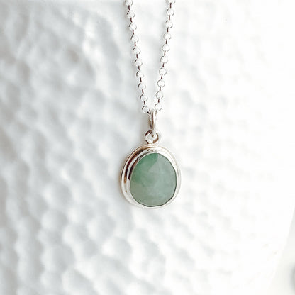 Close-up view of a pale aqua green rose-cut gandiderite and silver pendant on a white textured background.