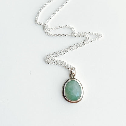 Seafoam green gandiderite and silver pendant with the chain organized in a zig zag pattern on a white background