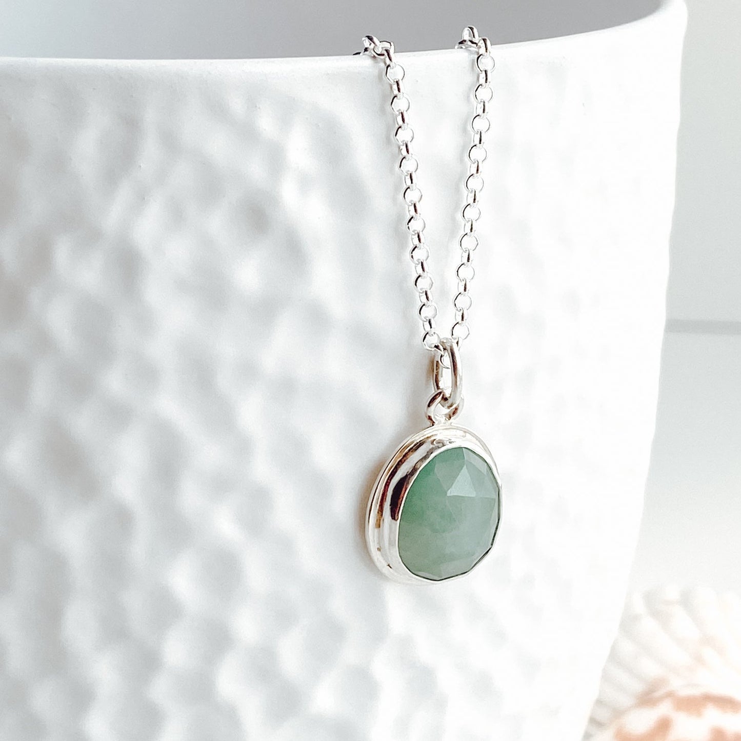 A close up view of an aqua green rose cut gandiderite gemstone pendant displayed on a textured white vase.