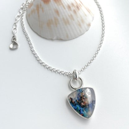 Chrysocolla in chalcedony trillion pendant in sterling silver on a white background with a sea shell