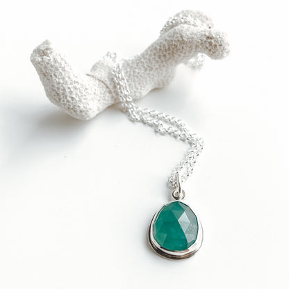 Blue-Green rosecut gemstone pendant displayed on a piece of white coral on a white background