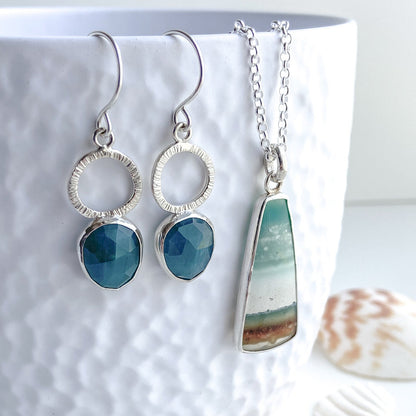 Teal green gandiderite drop earrings displayed with oblong opal wood beach scene pendant