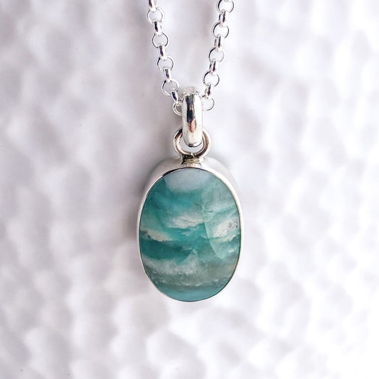 Close up view of the silver bezel set teal and aqua opalized wood gemstone pendant against a white textured background
