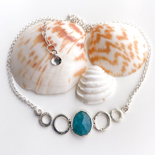 Blue-Green Gandiderite and textured silver oval necklace displayed on a white background with sea shells