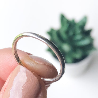 Fingers holding a plain silver stacking ring in front of a plant