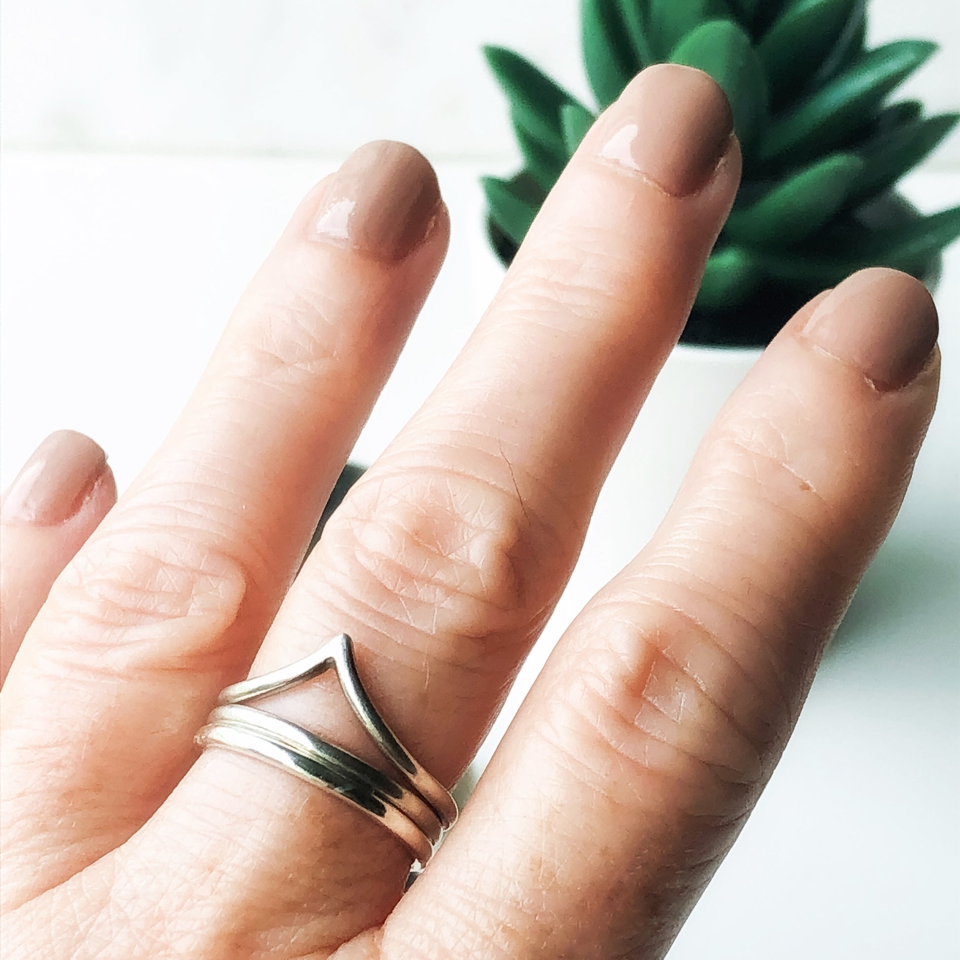 A hand with two plain stacking rings paired with the chevron ring