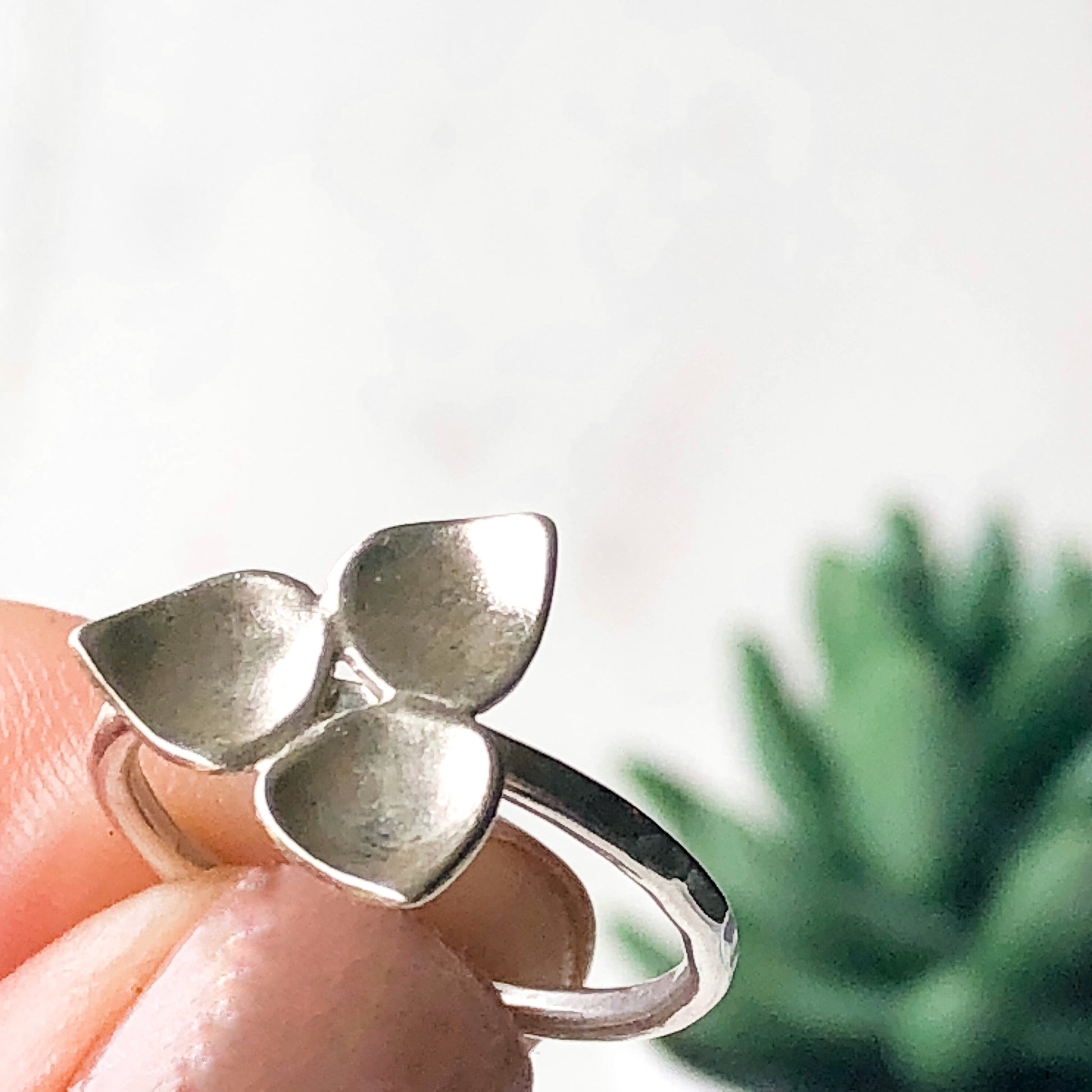 Silver trillium stacking ring help up in front of a plant